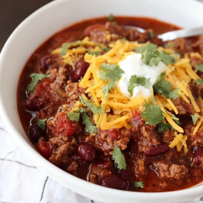 A hearty ladle of Beef and Bean Chili with Sharp Cheddar Cheese served alongside warm cornbread and tortilla chips.