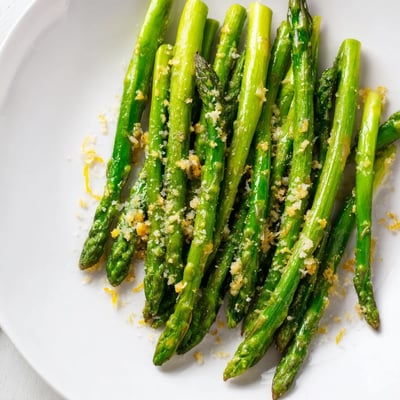 Tender crisp asparagus spears glistening with olive oil and lemon juice, plated warm as a vibrant Mediterranean side dish.
