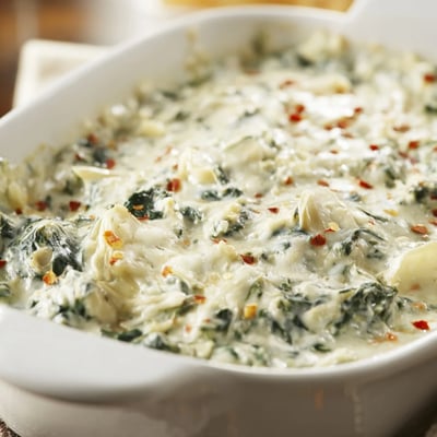 A freshly baked dish of Creamy Spinach and Artichoke Dip with a golden, cheesy crust and tender green specks.