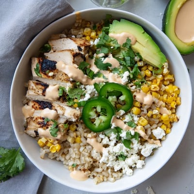 A hearty serving of Street Corn Chicken Bowl featuring sliced avocado, crumbled cotija, and fresh cilantro garnish.