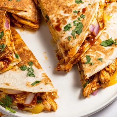 Serving hot honey BBQ chicken quesadillas with lime wedges, sour cream, and fresh cilantro garnish.