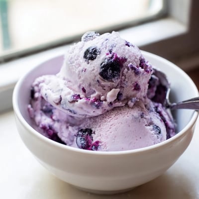 A food processor blending cottage cheese, heavy cream, and honey for Blueberry Cottage Cheese Ice Cream, with vibrant blueberries added for color and texture.